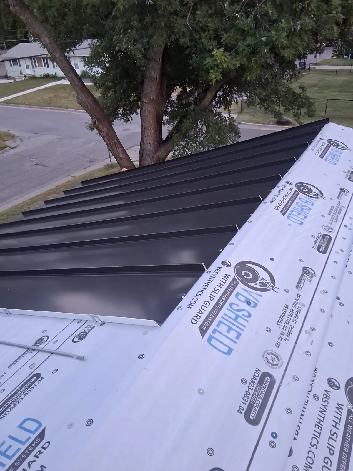 Standing seam metal panels partway up a roof over synthetic underlayment, ridge not yet closed