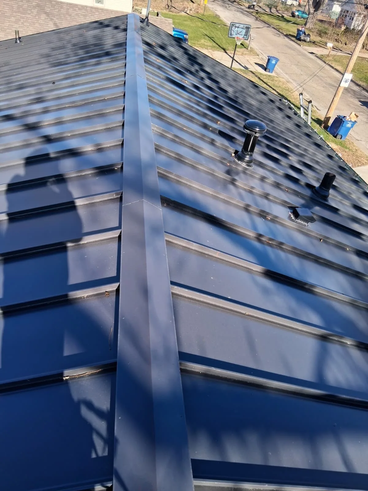 Finished standing seam metal roof with ridge cap, viewed from the ridge line down toward the street
