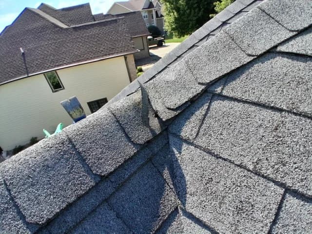 Lifted and detached ridge cap shingle on a roof, neighboring house in the background