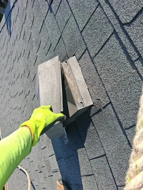 Gloved hand holding an old roof vent removed during a repair