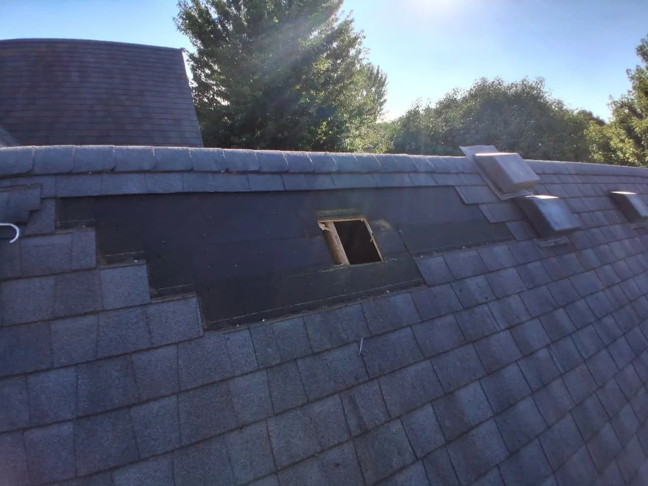 Long open strip under the ridge with felt exposed and a vent hole cut into the deck, old vents to the right