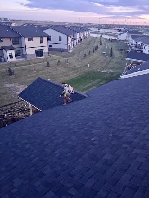 Roofer walking the ridge of a new shingle roof at dusk in a Des Moines metro subdivision