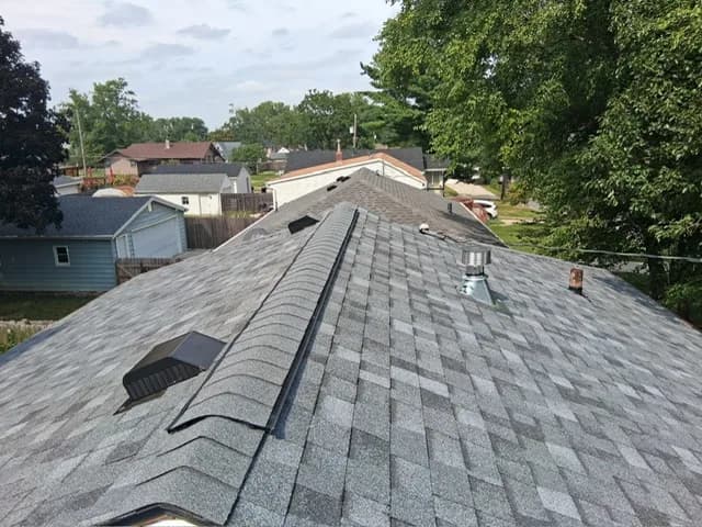 Finished gray architectural shingle roof viewed from the ridge down, with vent stacks and the neighborhood behind it, Des Moines