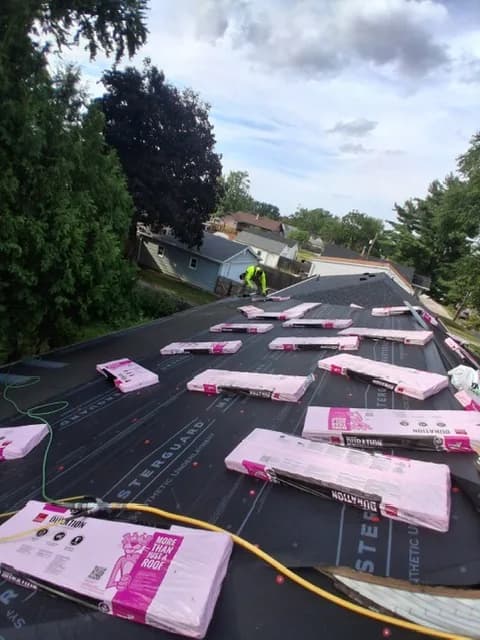 Owens Corning Duration shingle bundles stacked on synthetic underlayment during a Des Moines tear-off, roofer working in the background