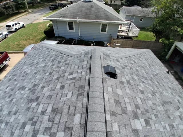 Finished architectural shingle roof from above, chimney flashing and roof vent visible on the slope, Des Moines