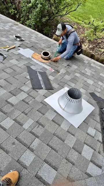 Roofer setting a new pipe boot flashing into the shingle field around a vent pipe