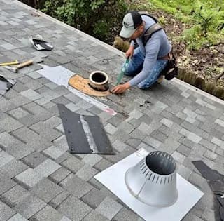 Roofer cutting in new flashing around a vent pipe on a shingle roof, old flashing removed nearby